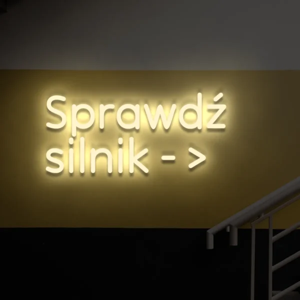 Beżowy neon LED z napisem „Sprawdź silnik →” na ścianie